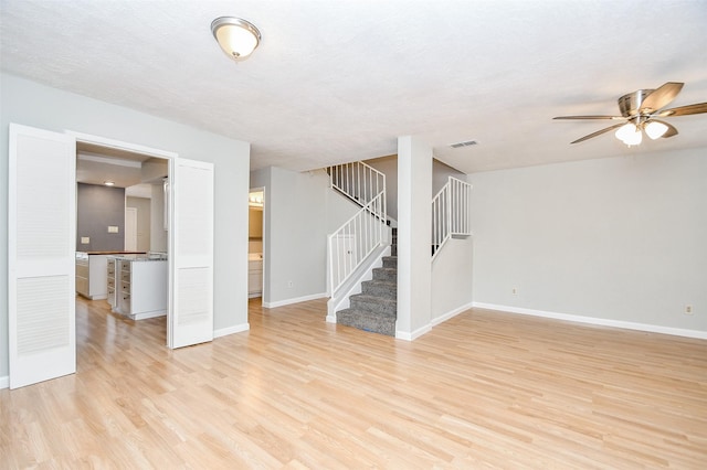 basement featuring ceiling fan, light wood-type flooring, and a textured ceiling