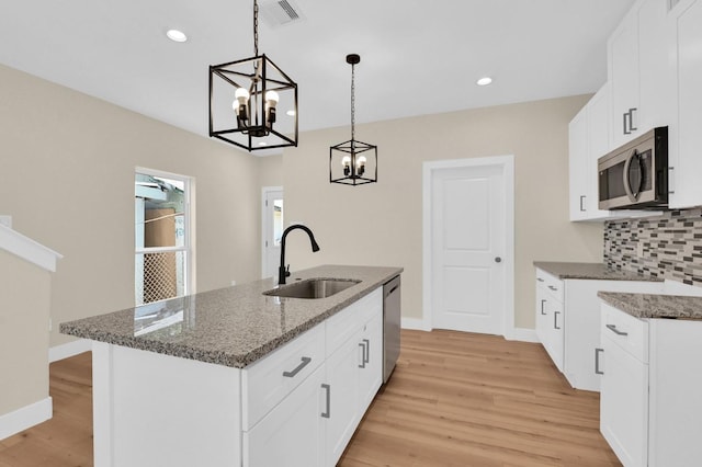 kitchen featuring appliances with stainless steel finishes, sink, white cabinetry, hanging light fixtures, and an island with sink