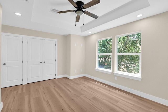 unfurnished bedroom featuring light hardwood / wood-style floors, a raised ceiling, and ceiling fan