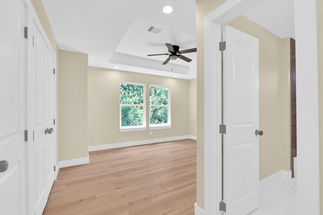 unfurnished bedroom featuring ceiling fan, light hardwood / wood-style floors, and a raised ceiling