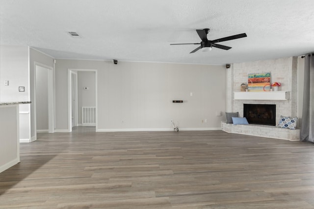 unfurnished living room with ceiling fan, hardwood / wood-style floors, a textured ceiling, and a brick fireplace