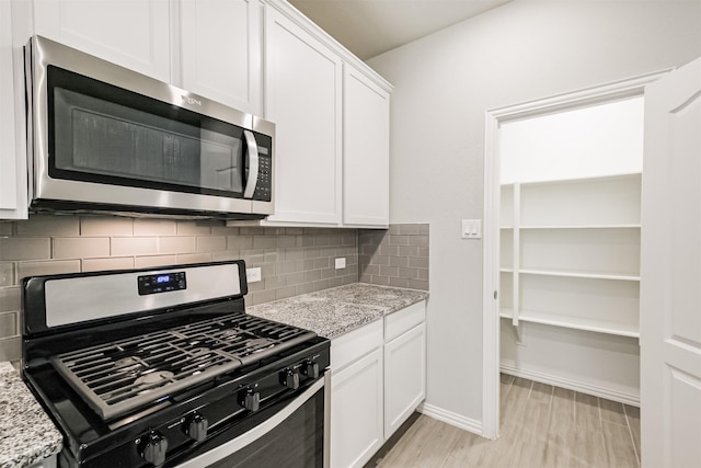 kitchen featuring white cabinetry, light stone countertops, backsplash, light hardwood / wood-style floors, and appliances with stainless steel finishes