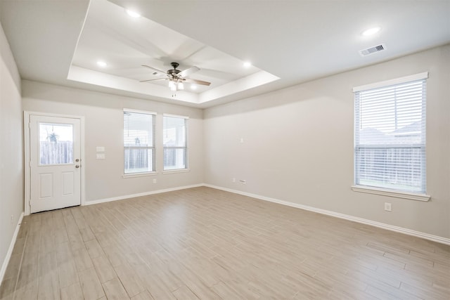 spare room featuring light wood-type flooring, a tray ceiling, and plenty of natural light