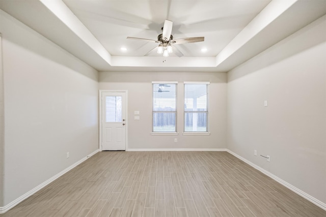 empty room featuring ceiling fan, light wood-type flooring, and a tray ceiling