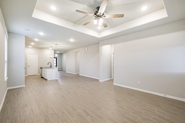 unfurnished living room featuring ceiling fan, light hardwood / wood-style floors, and a tray ceiling