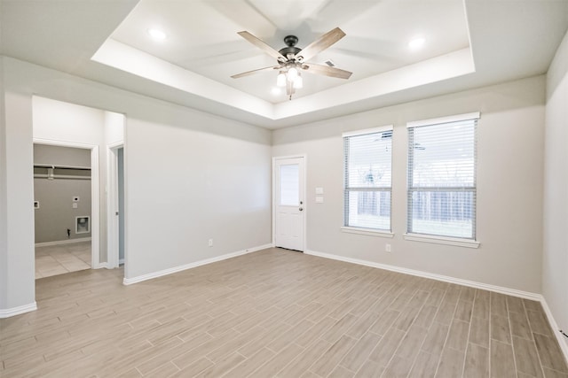 unfurnished room with a raised ceiling, ceiling fan, and light hardwood / wood-style floors