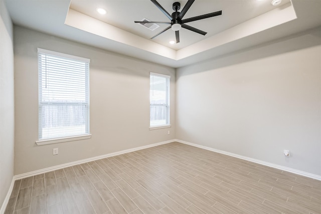 unfurnished room featuring a tray ceiling, light hardwood / wood-style flooring, and plenty of natural light