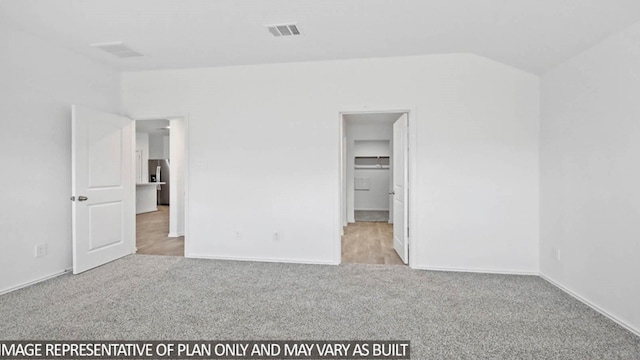 unfurnished bedroom featuring light carpet, a spacious closet, and lofted ceiling