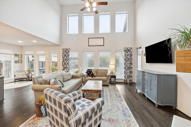 living room featuring a healthy amount of sunlight, dark hardwood / wood-style flooring, ceiling fan, and a high ceiling