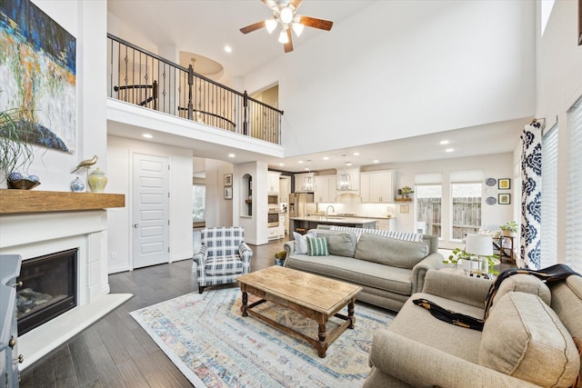 living room featuring a high ceiling, dark wood-type flooring, sink, and ceiling fan