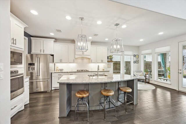 kitchen with stainless steel appliances, sink, white cabinets, an island with sink, and hanging light fixtures