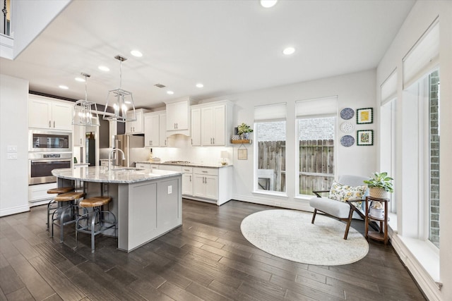 kitchen with decorative light fixtures, white cabinetry, an island with sink, and appliances with stainless steel finishes