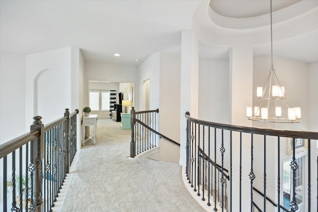 hallway with a raised ceiling, an inviting chandelier, and light carpet