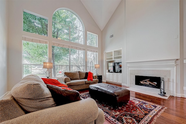 living room featuring a towering ceiling, wood-type flooring, a tile fireplace, and built in features