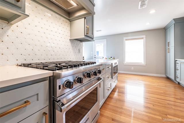 kitchen featuring gray cabinets, tasteful backsplash, built in microwave, high end stainless steel range, and light hardwood / wood-style floors