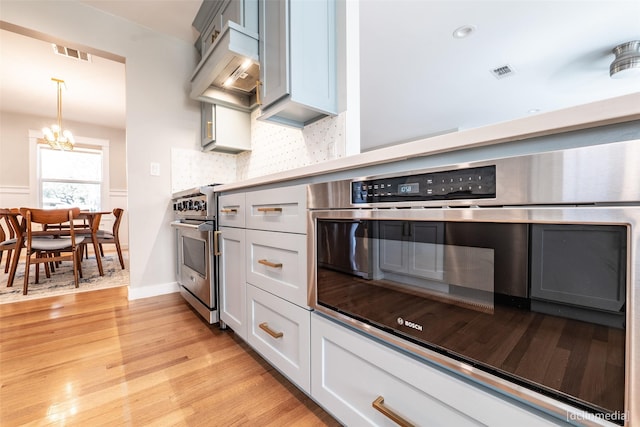 kitchen featuring light hardwood / wood-style flooring, appliances with stainless steel finishes, premium range hood, backsplash, and a notable chandelier