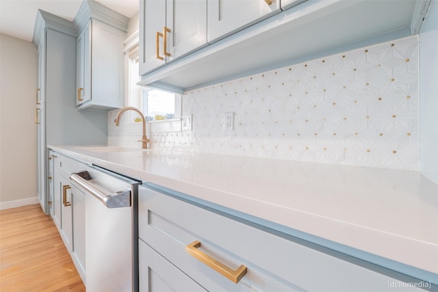 kitchen featuring tasteful backsplash, sink, stainless steel dishwasher, and light hardwood / wood-style flooring