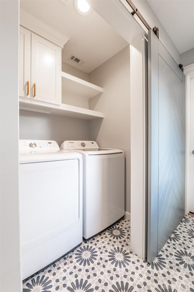 clothes washing area featuring cabinets, a barn door, light tile patterned floors, and washing machine and clothes dryer