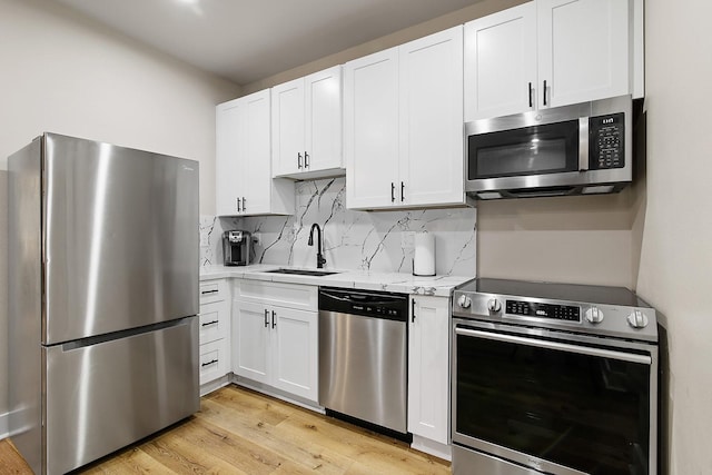 kitchen featuring light stone countertops, stainless steel appliances, tasteful backsplash, white cabinets, and light wood-type flooring