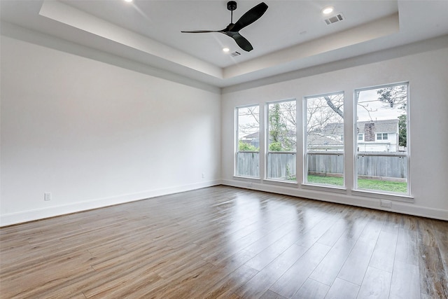 empty room with a tray ceiling, light hardwood / wood-style flooring, and ceiling fan