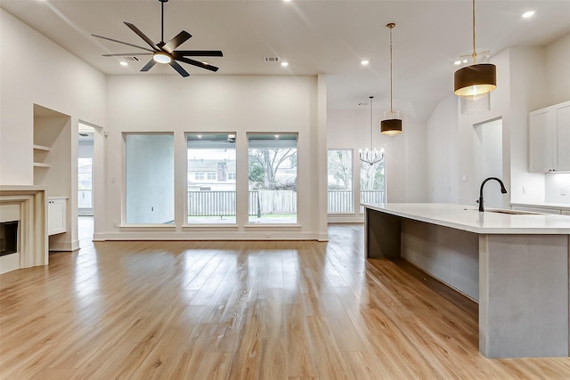 kitchen with a large island with sink, ceiling fan with notable chandelier, hanging light fixtures, built in features, and a healthy amount of sunlight