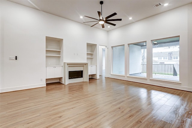 unfurnished living room featuring built in shelves, light wood-type flooring, and ceiling fan