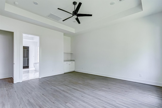 empty room featuring light wood-type flooring, a tray ceiling, and ceiling fan