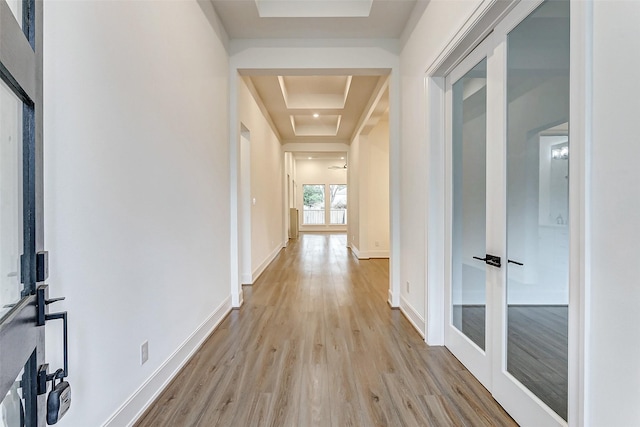 hallway featuring a tray ceiling, french doors, and light hardwood / wood-style floors