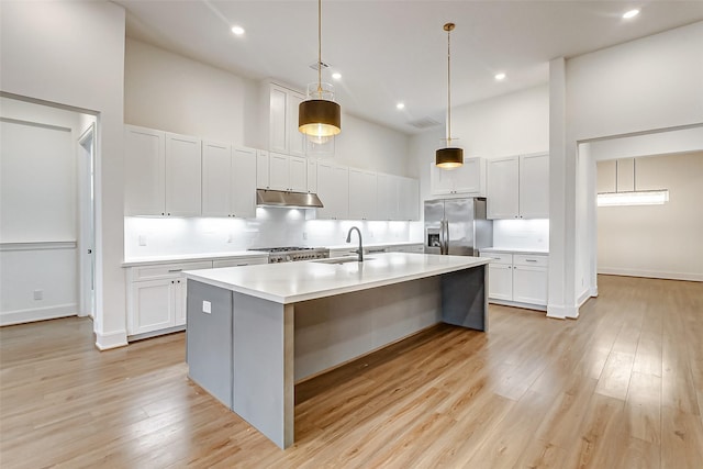 kitchen with stainless steel fridge, a kitchen island with sink, pendant lighting, a high ceiling, and white cabinetry