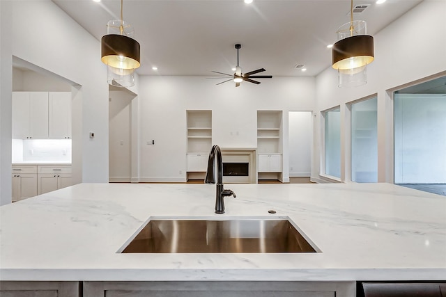 kitchen featuring ceiling fan, light stone counters, hanging light fixtures, and sink