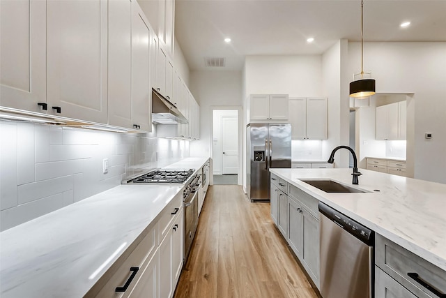 kitchen with light stone countertops, sink, decorative light fixtures, white cabinets, and appliances with stainless steel finishes