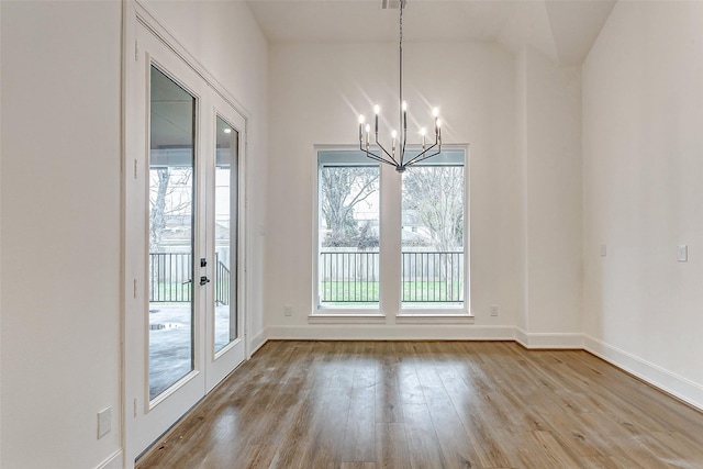 unfurnished dining area featuring french doors, light hardwood / wood-style flooring, and a notable chandelier