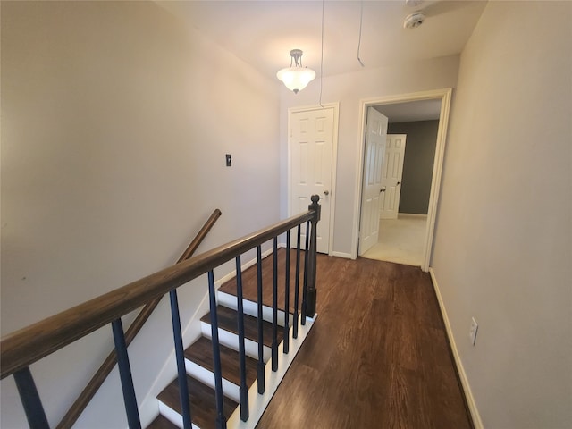 hallway with dark wood-style flooring, baseboards, and an upstairs landing
