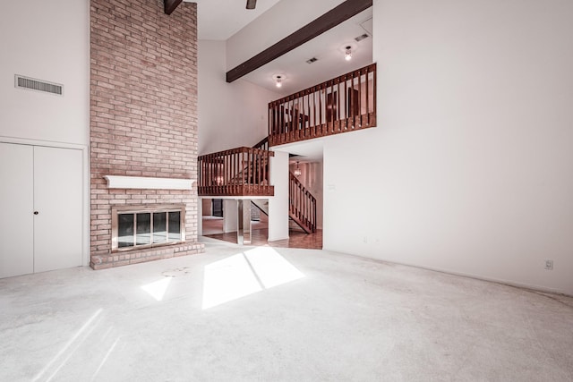 unfurnished living room with a high ceiling, beamed ceiling, a fireplace, and carpet flooring