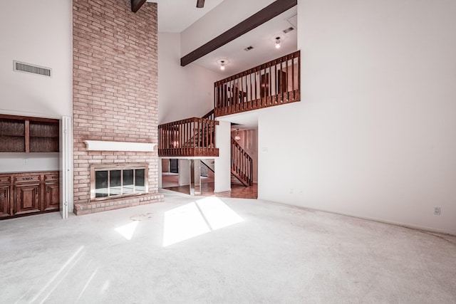 unfurnished living room featuring a high ceiling, a brick fireplace, carpet floors, and beamed ceiling