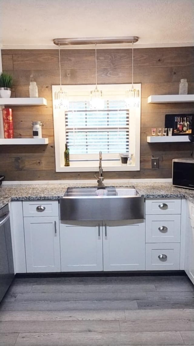 kitchen with white cabinets, wood walls, and hanging light fixtures