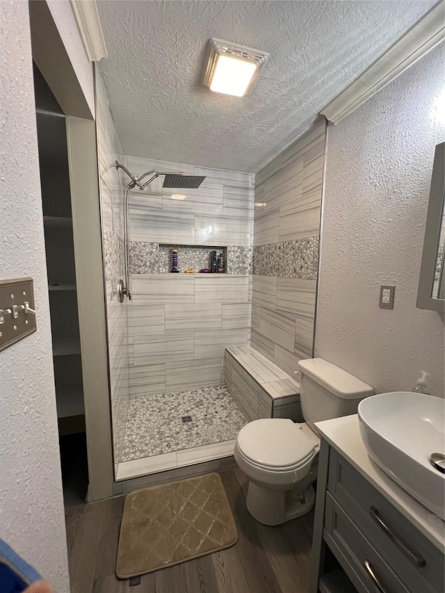 bathroom with a tile shower, vanity, a textured ceiling, hardwood / wood-style flooring, and toilet