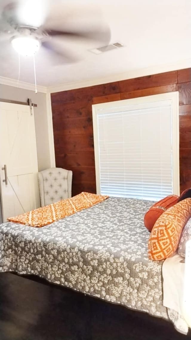 bedroom with ceiling fan, a barn door, crown molding, and wooden walls