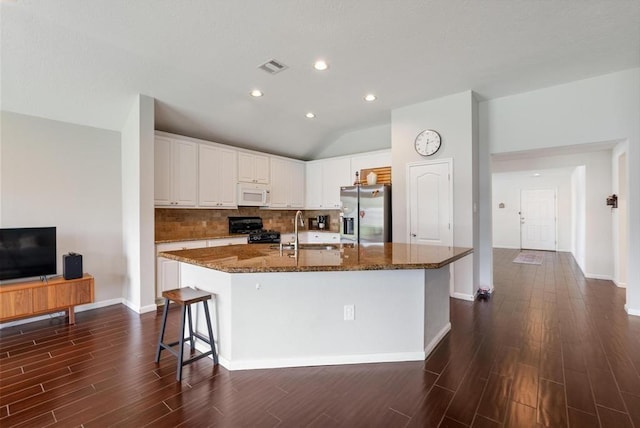 kitchen featuring dark stone counters, black range with gas stovetop, a spacious island, white cabinets, and stainless steel fridge with ice dispenser