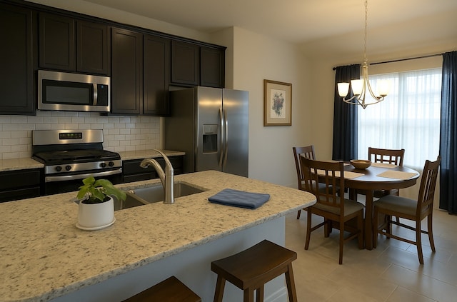 kitchen with light stone countertops, appliances with stainless steel finishes, an inviting chandelier, a sink, and decorative backsplash
