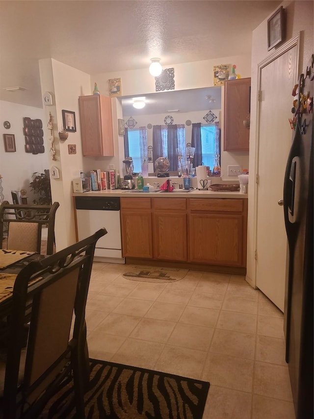 kitchen with light tile patterned floors, a textured ceiling, white dishwasher, and stainless steel refrigerator