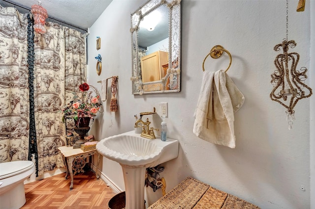 bathroom featuring toilet, sink, parquet floors, and a textured ceiling