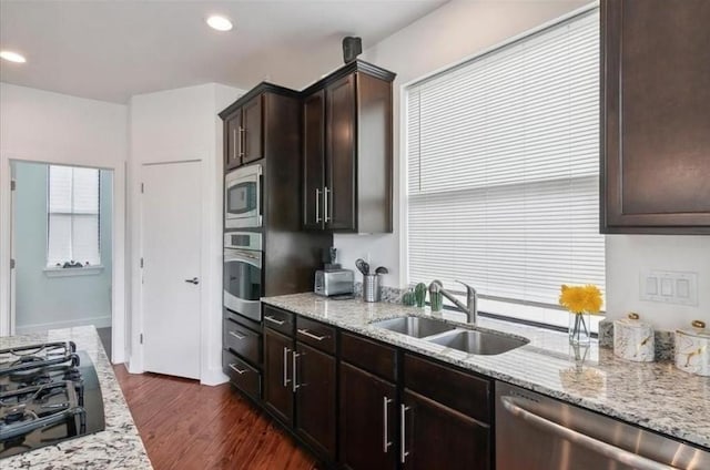 kitchen with stainless steel appliances, light stone counters, dark hardwood / wood-style floors, dark brown cabinetry, and sink