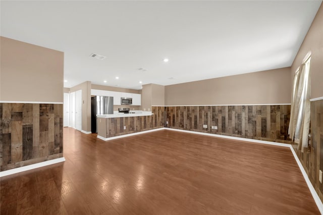 unfurnished living room featuring dark wood-type flooring and wood walls