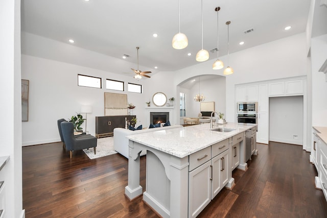 kitchen with light stone counters, a kitchen island with sink, sink, decorative light fixtures, and white cabinetry