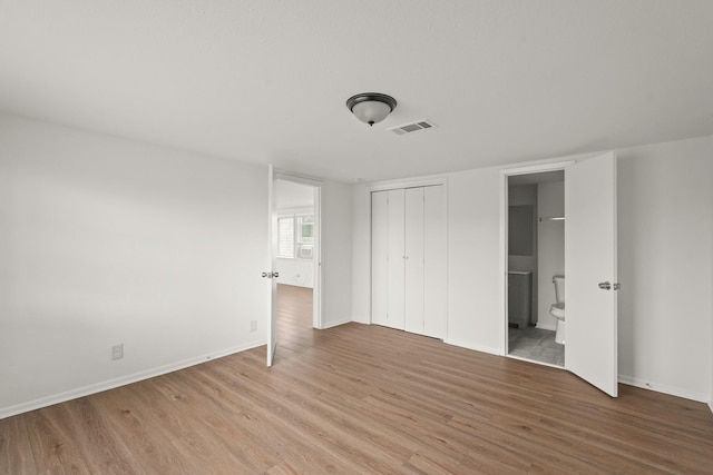 unfurnished bedroom featuring ensuite bathroom and wood-type flooring