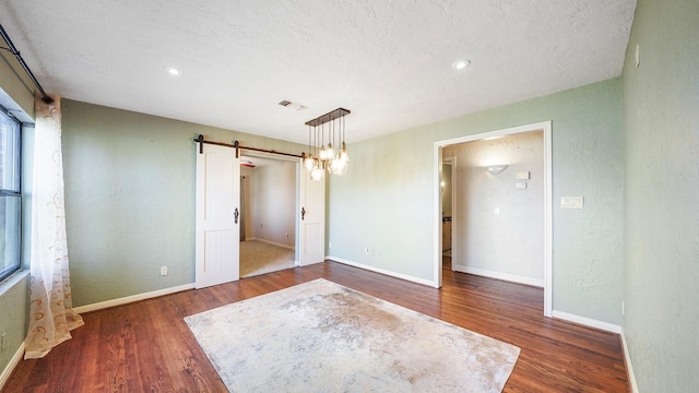 empty room with a barn door, dark hardwood / wood-style flooring, and a textured ceiling