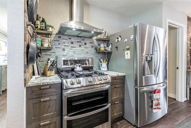 kitchen featuring backsplash, light stone counters, wall chimney exhaust hood, and stainless steel appliances