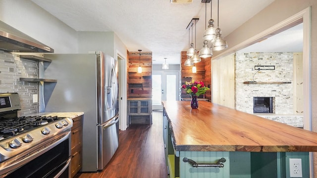 kitchen with wood counters, tasteful backsplash, stainless steel gas range oven, wall chimney exhaust hood, and hanging light fixtures