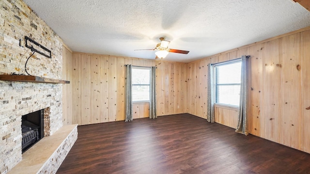 unfurnished living room featuring a textured ceiling, ceiling fan, wooden walls, dark wood-type flooring, and a fireplace